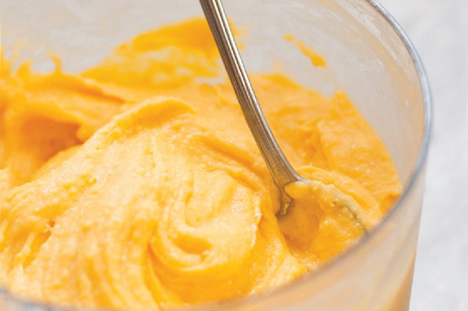 A closeup of a food processor container full of Mango, Lime, and Cream Cheese Sherbet.