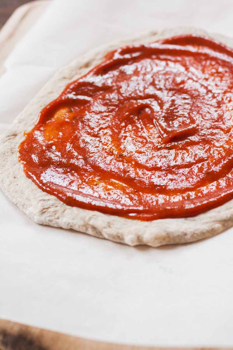 Raw pizza dough with sauce smeared on top.