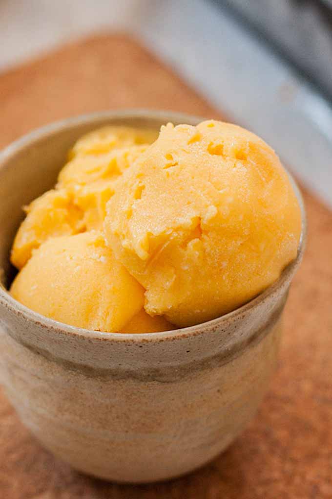 A closeup of an earthenware cup full of mango-lime and cream cheese sherbet.