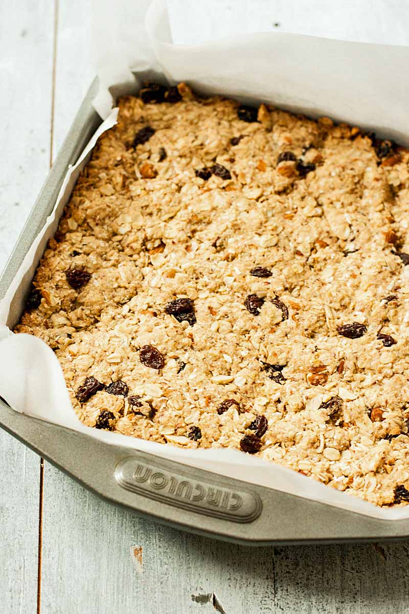 Uncut vegan oatmeal breakfast bars in a 8x8-inch baking pan sitting on a whitewashed wooden table. Closeup image.