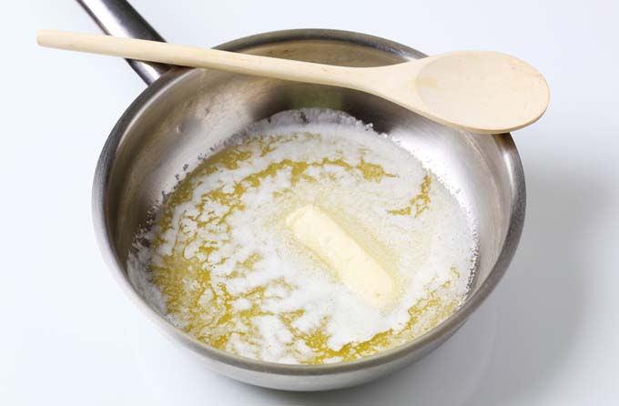 A saucepan of melting butter with a wooden spoon resting on the rim, to make a sauce.