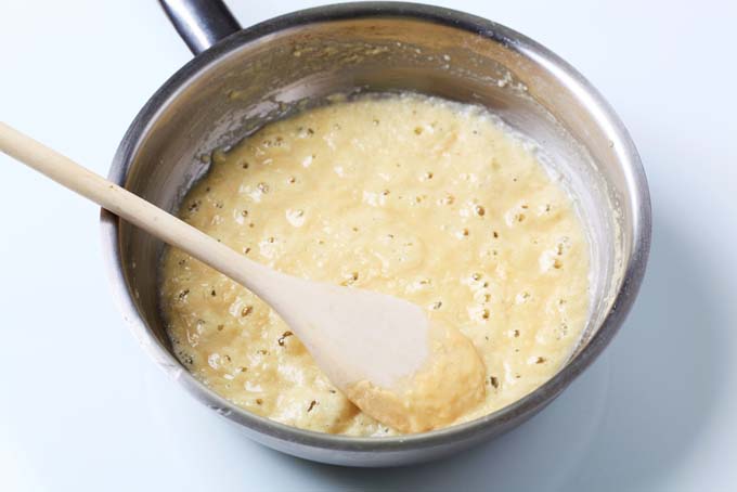 A pan of bubbling blonde roux, being stirred with a wooden spoon.