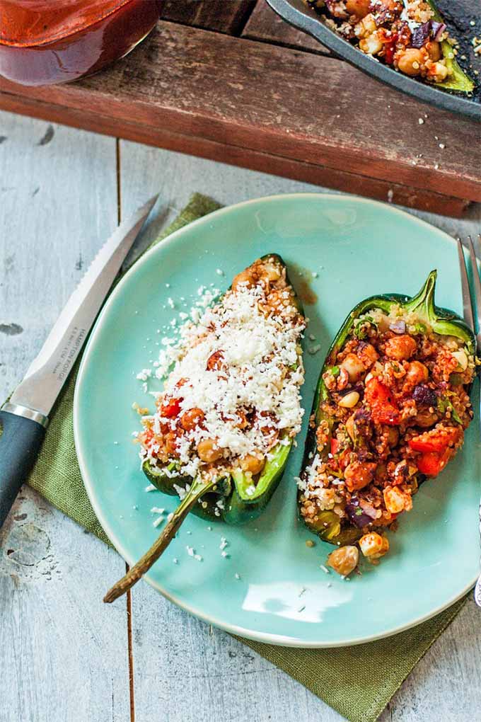 Top-down view of a grilled poblano cut in half, and stuffed with a mixture of quinoa, corn, bell pepper, and onion, topped with red enchilada sauce and crumbled cotija cheese.