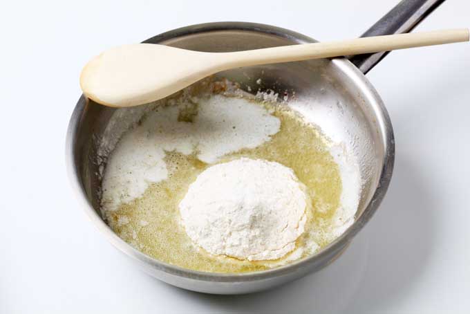 Melted butter in a saucepan with a pile of white flour on top, to make a sauce, with a wooden spoon resting on the rim of the pan.