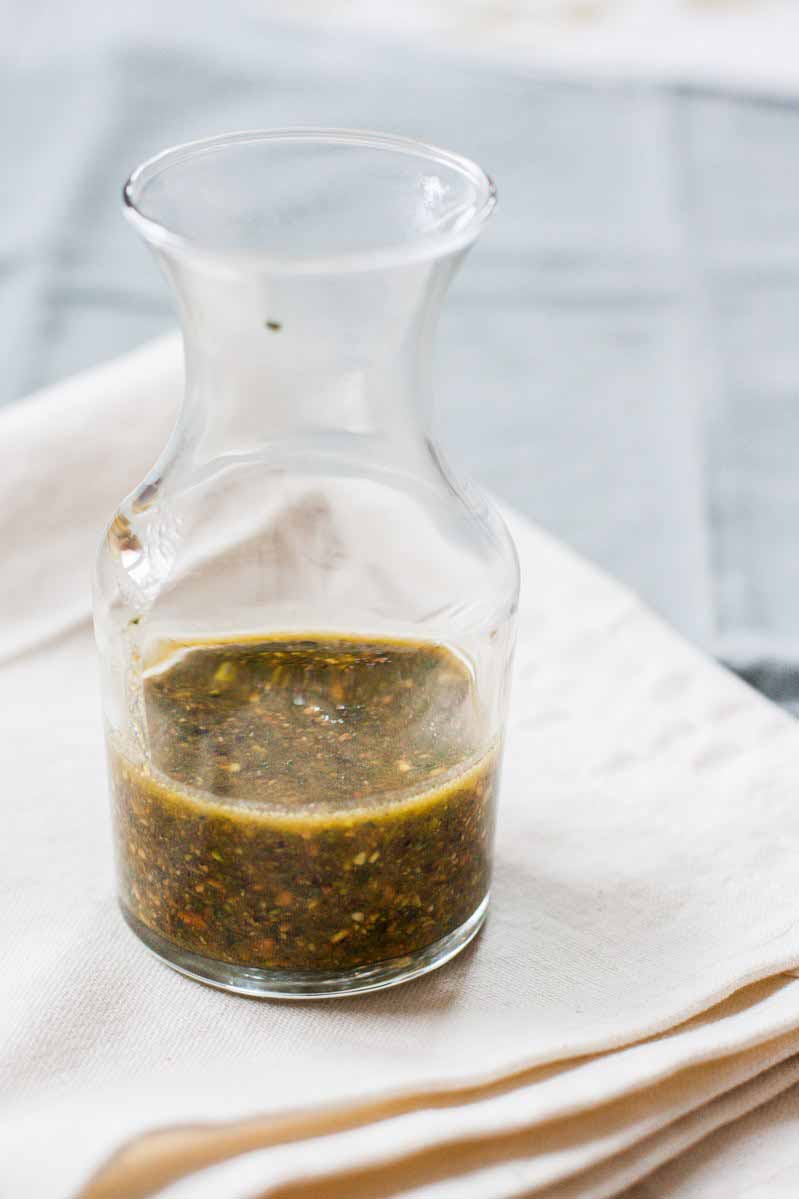 A clear glass jar full of a pesto sauce made with pistachios and fresh basil.