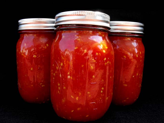 Three big jars of canned tomatoes, stewed, sauced, chopped. Home food canning and crafts or homemade style tomato recipes.