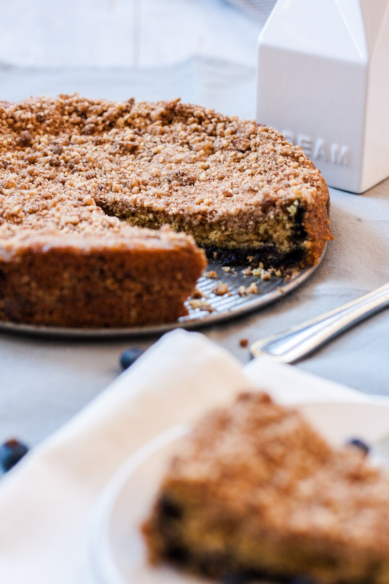 Selective focus and oblique shot of healthy vegan blueberry coffee cake. The cake is in the background with clear focus. A slice is in the foreground with diffused focus.