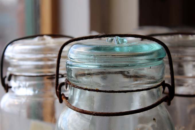 Three old glass mason jars on windowsill with rusty tops.