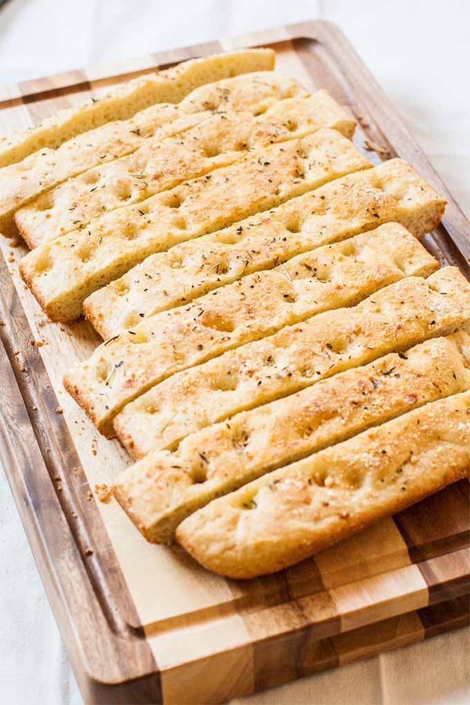 A flat loaf of focaccia, cut into long, narrow slices that are arranged on a wood cutting board.