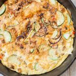 Top-down shot of a potato and zucchini egg frittata in a cast iron pan, golden brown on top, on a distressed wood background.