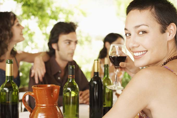 Portrait of happy young woman enjoying red wine with friends in background