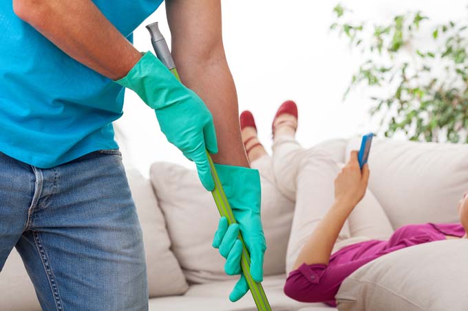 man cleaning while woman relaxes on couch
