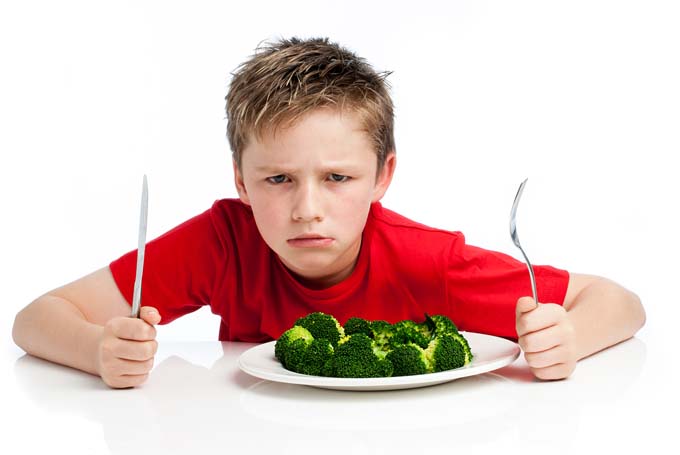 Grouchy young boy with plate of broccoli.