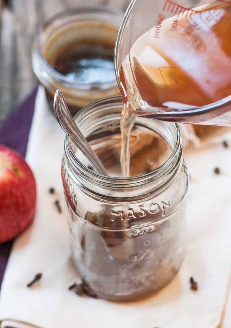 Apple cider being poured into a large mason jar that already contains caramel sauce.