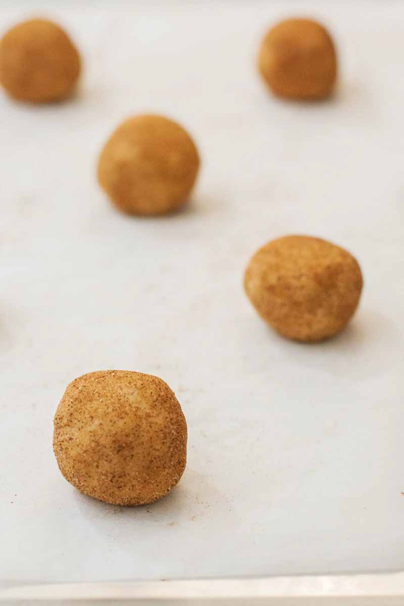 Five small balls of dough coated in cinnamon sugar, on white parchment paper.