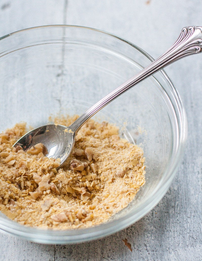 A vegan Parmesan substitute made with nutritional yeast and walnut pieces in a small glass mixing bowl.