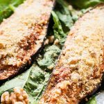 Close up of two halves of a marinara stuffed and roasted eggplant halves on a bed of leaf lettuce.