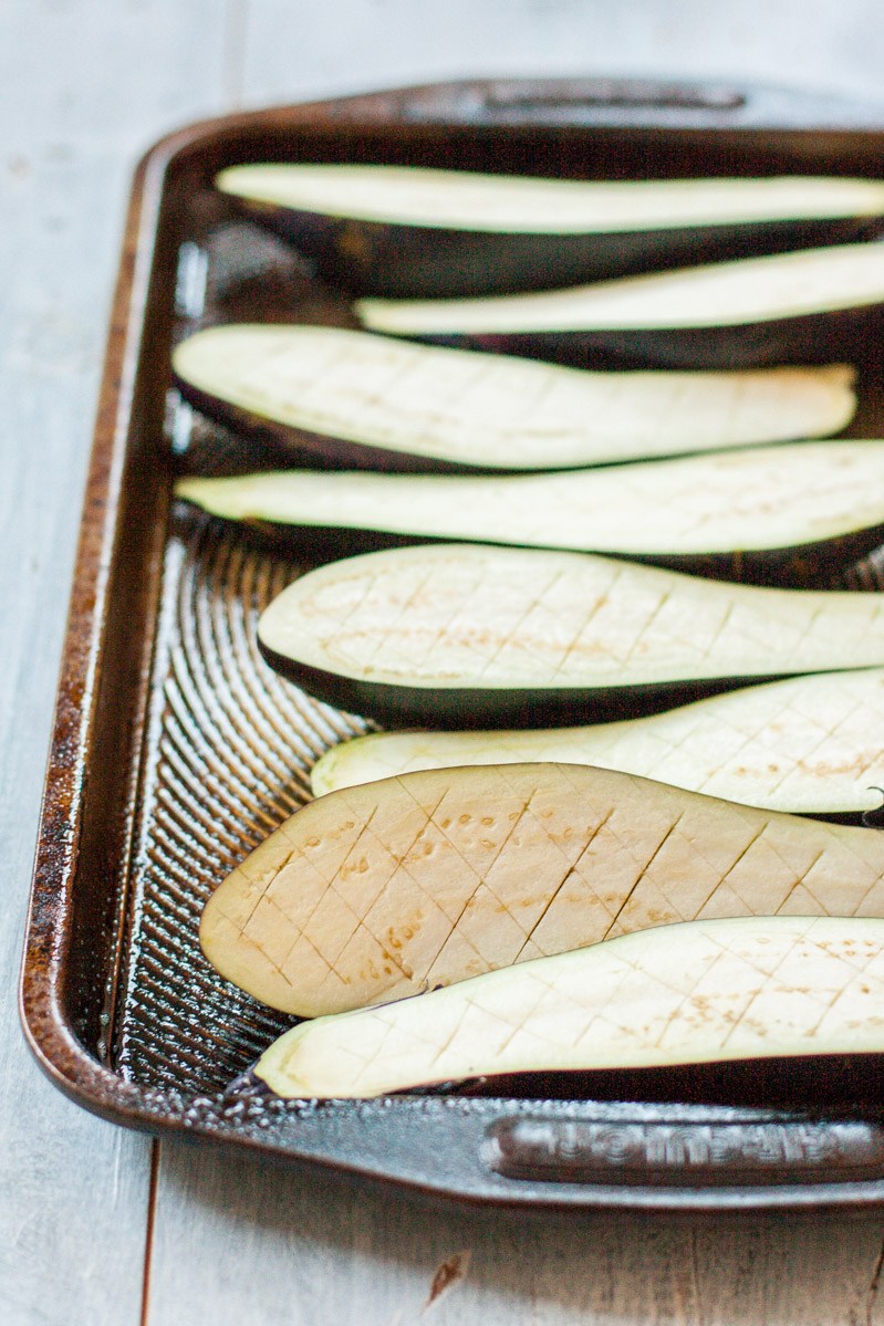 Top down, slightly oblique view of Japanese eggplant halves on a rimmed baking sheet. 