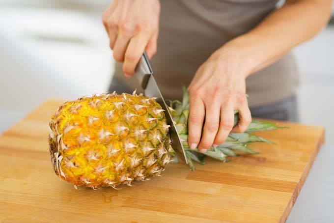 The crown of a pineapple being sliced off in order to prepare and serve