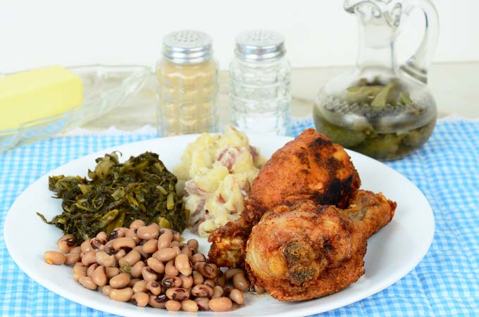 Southern fried chicks, turnip greens, black eed peas, fried potatoes and collard greens; on a blue and white checked table cloth; pepper, salt and sweet sourthen tea in background