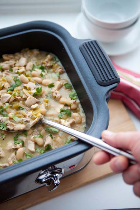 White Chicken Chili in slow cooker; human hand dipping spoonful out