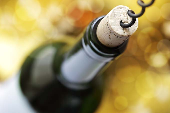 A corkscrew enters the cork in the top of a bottle of wind; defocused background
