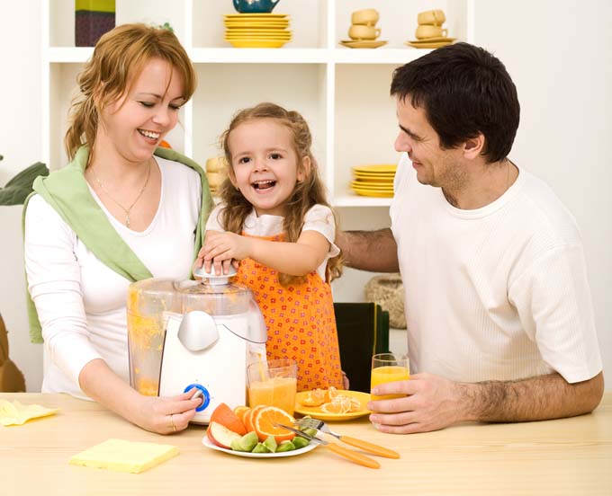 A mother, father, and you girl gather around a juicer on the kitchen table