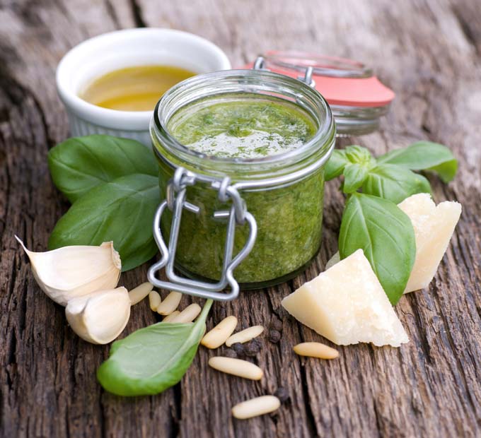 Pesto sauce on rustic wooden table with pine nuts and basil leaves scattered around