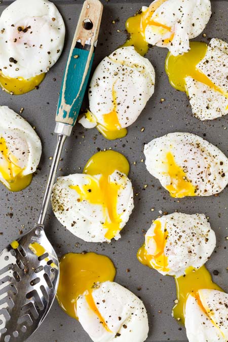 A dozen poached eggs on a granite countertop with yolks oozing out; slotted spoon resting on top.