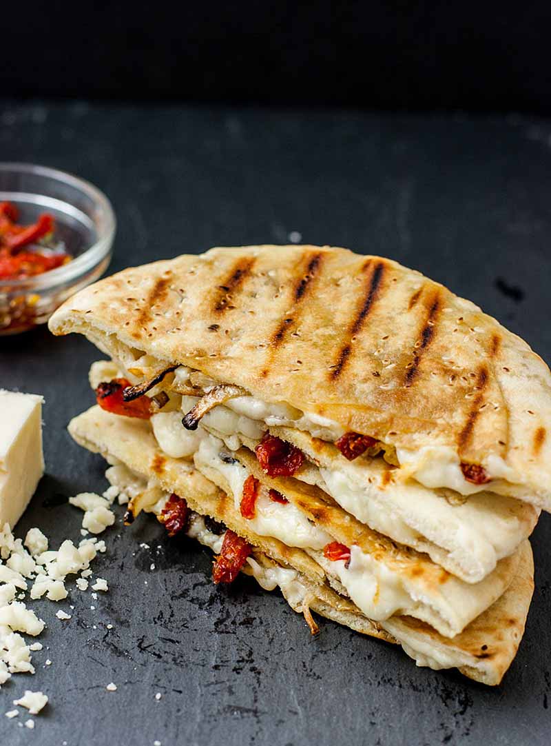 Oblique view of a grilled cheese pita made with white cheddar cheese, sundried tomatoes, and caramelized onions.