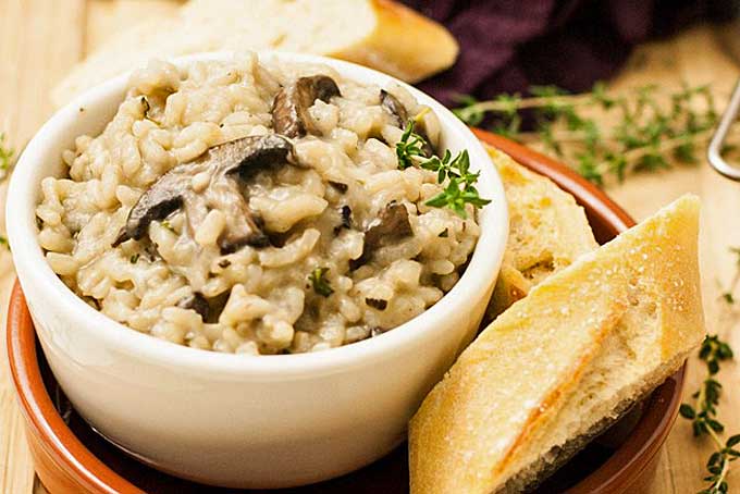 Close up of a white ceramic bowl full of vegan mushroom and herb risotto rice.