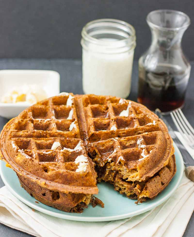 Oblique view of two sweet potato waffles with vegan margarine on top, and with a large bite cut out.