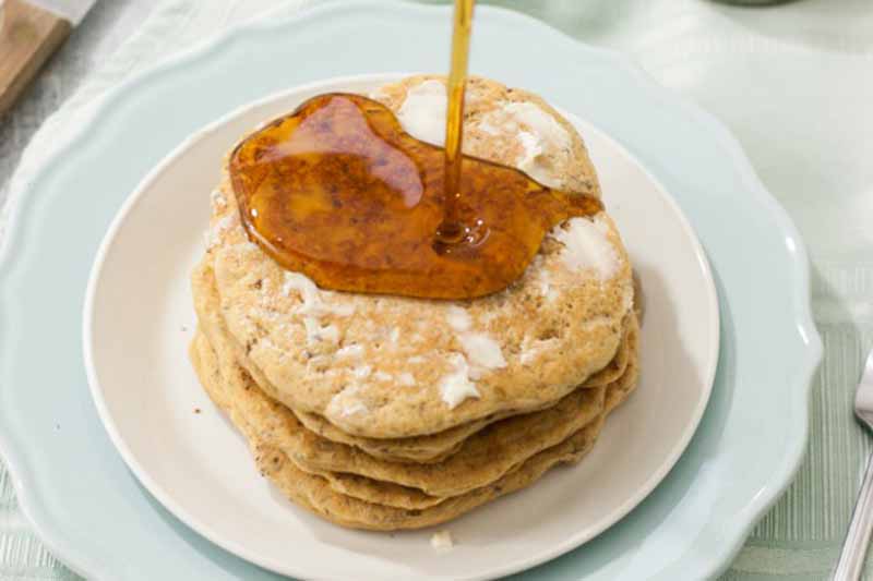 Horizontal image of vegan hotcakes with syrup poured on top of them.