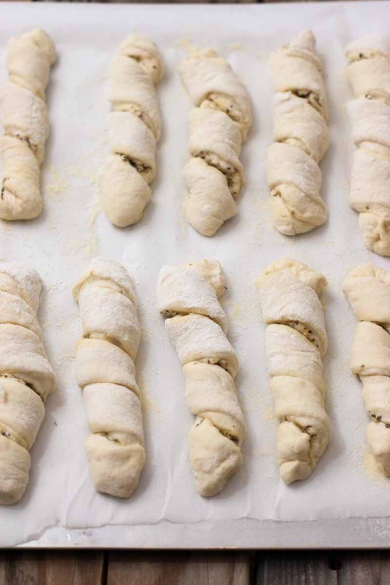 Top down view of a batch of unbaked Italian breadstick twists on a baking sheet lined with parchment paper.