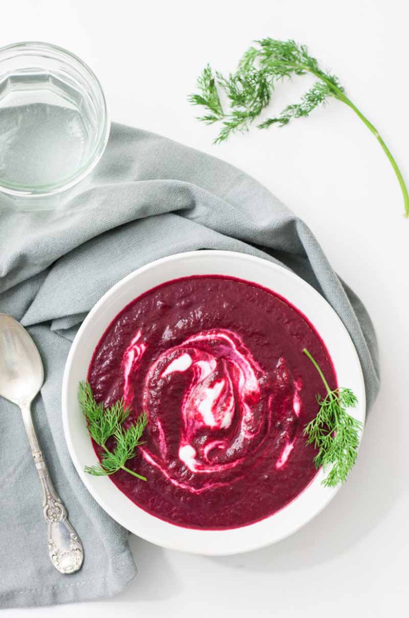 Top down view of a white ceramic bowl containing a deep purple roasted beet soup with cashew cream topping.