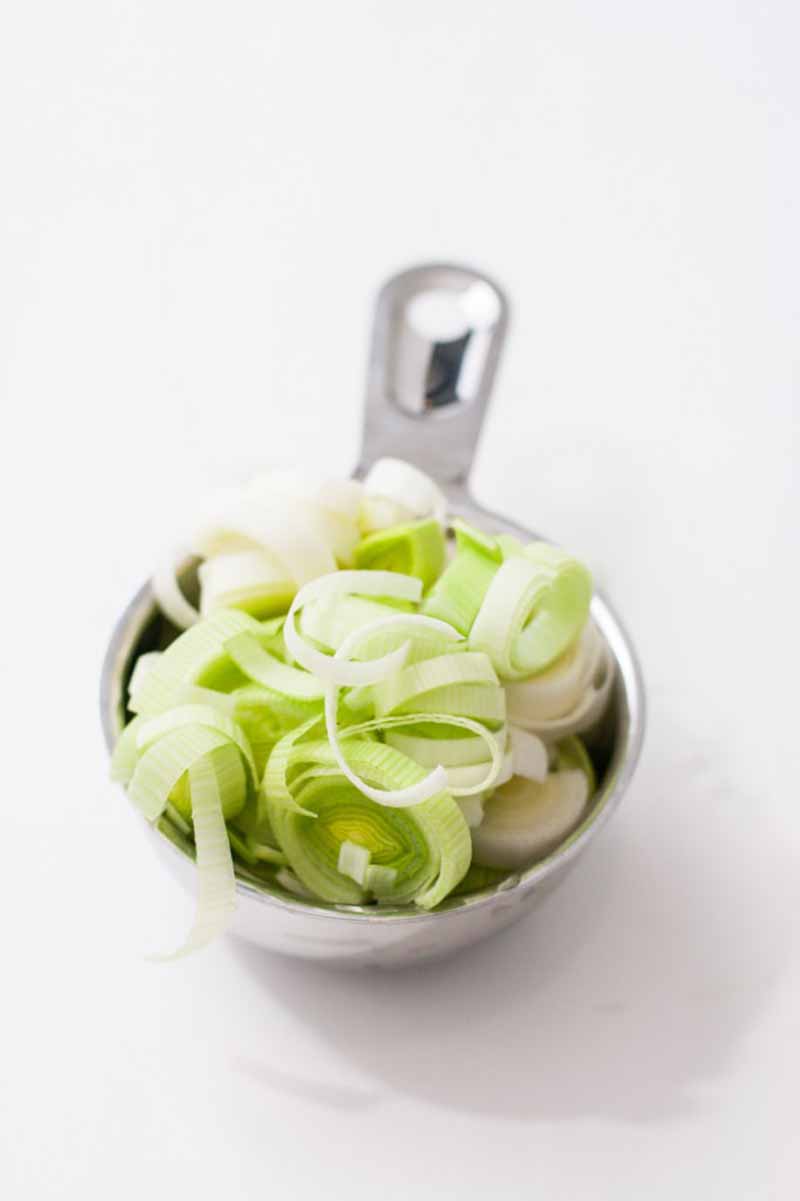 Oblique view of sliced shallots and leeks inside of measuring cup on a white background.