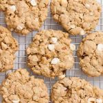 Top down view of a group of vegan white chocolate hazelnut oatmeal cookies placed on a stainless steel cooling rack.