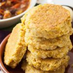 Oblique stack of a vegan-friendly cornbread skillet biscuit recipe stacked inside of a brown, ceramic bowl