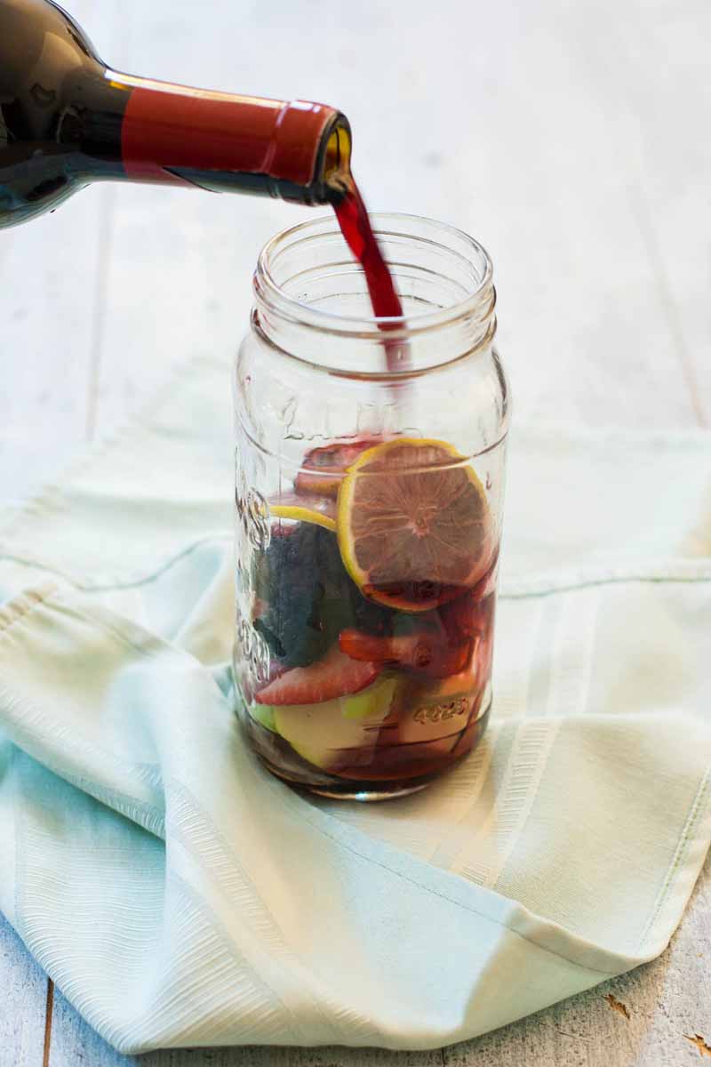 Red wine being poured in a mason jar over mixed fresh fruit and berries.
