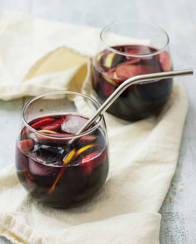 Close up of two low ball glasses filled full of a homemade sangria cocktail over ice.