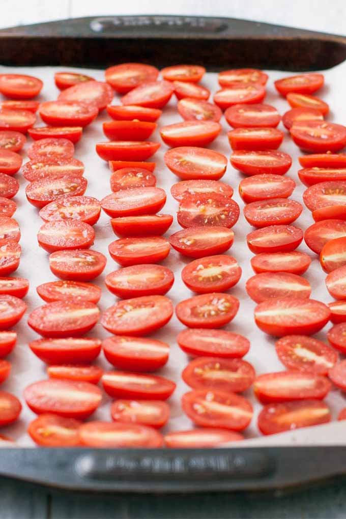 Fresh red grape tomatoes cut in half and arranged in six rows on a baking sheet lined with parchment paper.