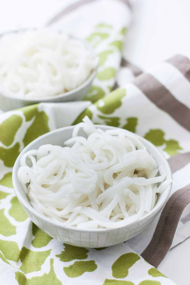 Vertical image of a bowl of white noodles in a white bowl on a green patterned napkin.