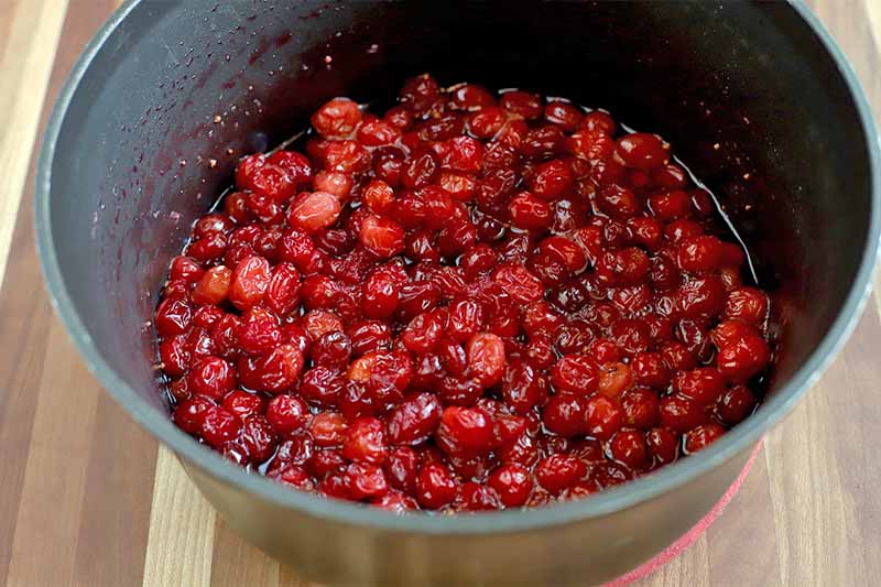 Whole cooked cranberries in a nonstick pan, on a wood surface.