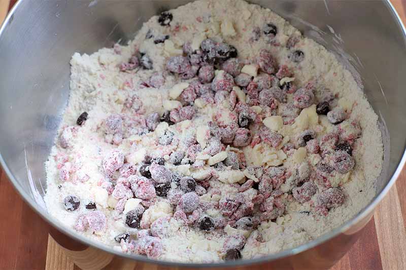 Chopped fresh cranberries and chocolate chips coated in a flour mixture in a stainless steel mixing bowl.