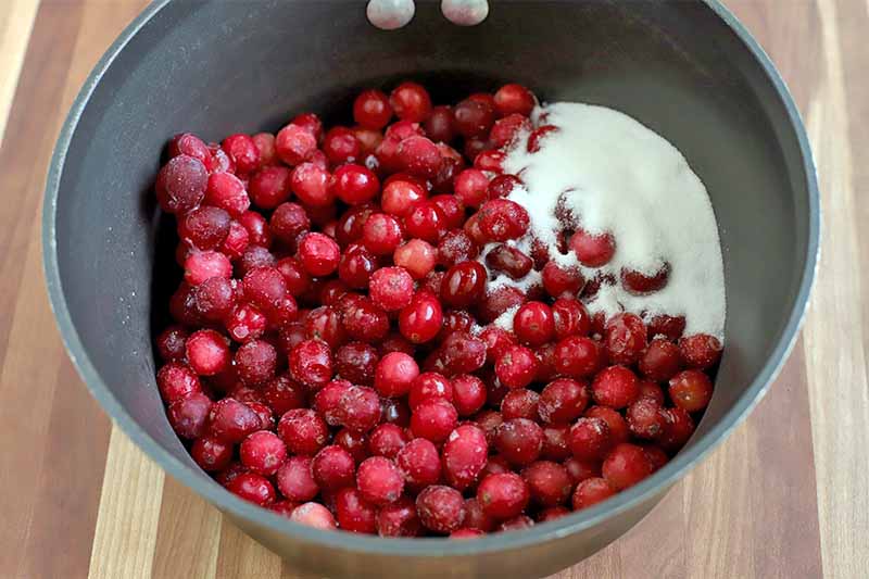 A nonstick stock pot of whole cranberries and sugar, on a wood background.