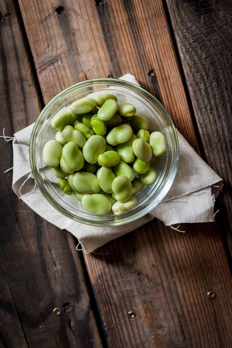 Vertical image of a glass bowl with fava beans.