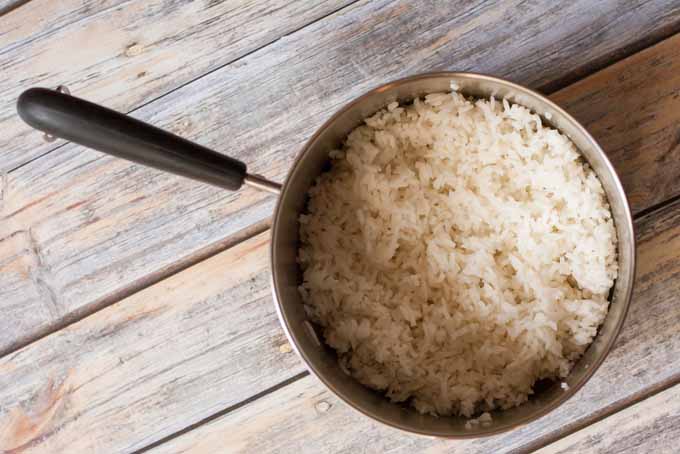 Top down view of a sauce pan full of fluffed, cooked rice on a weathered wooden surface.