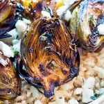 Closeup of grilled baby artichokes on a bed of brown rice with crumbled feta and fresh thyme.