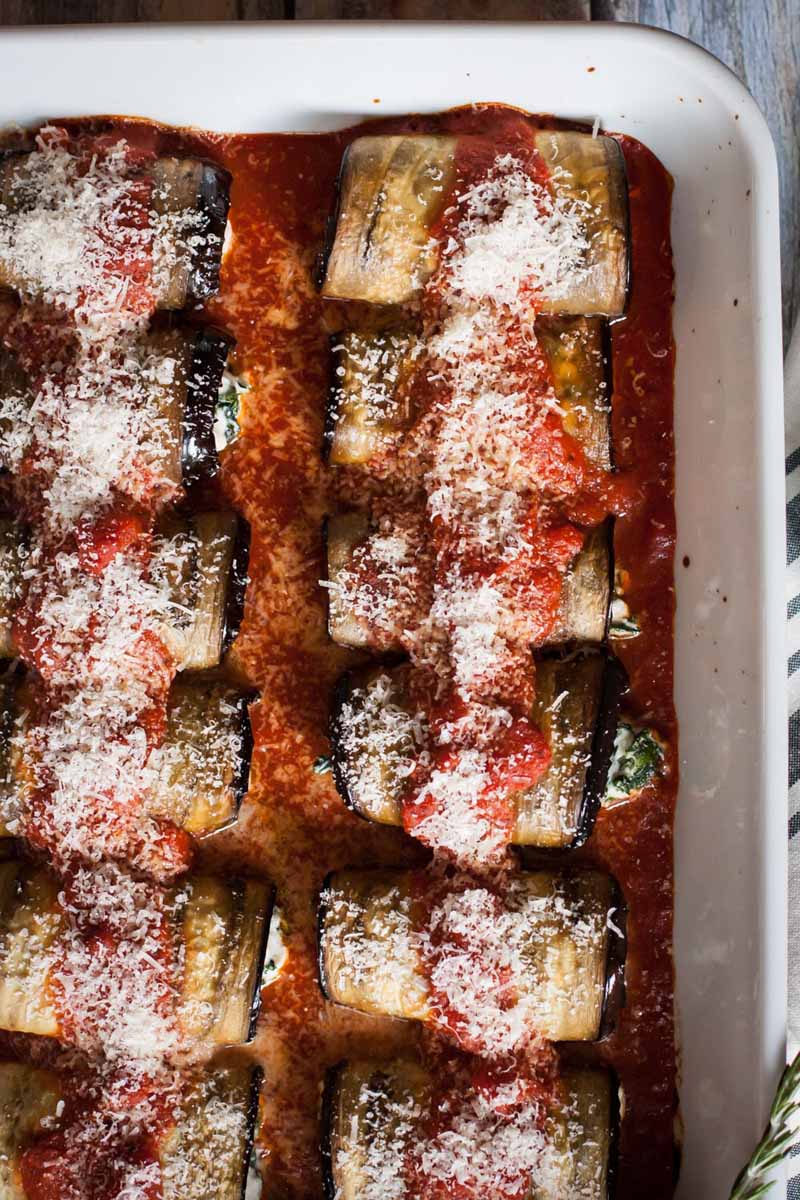 Top down view of gluten-free Eggplant, Kale & Ricotta Cannelloni recipe in a white ceramic casserole dish. Fully baked with freshly grated Parmesan cheese grated on top.