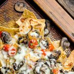 Closeup of a brown baking pan of homemade nachos, on a wood background.